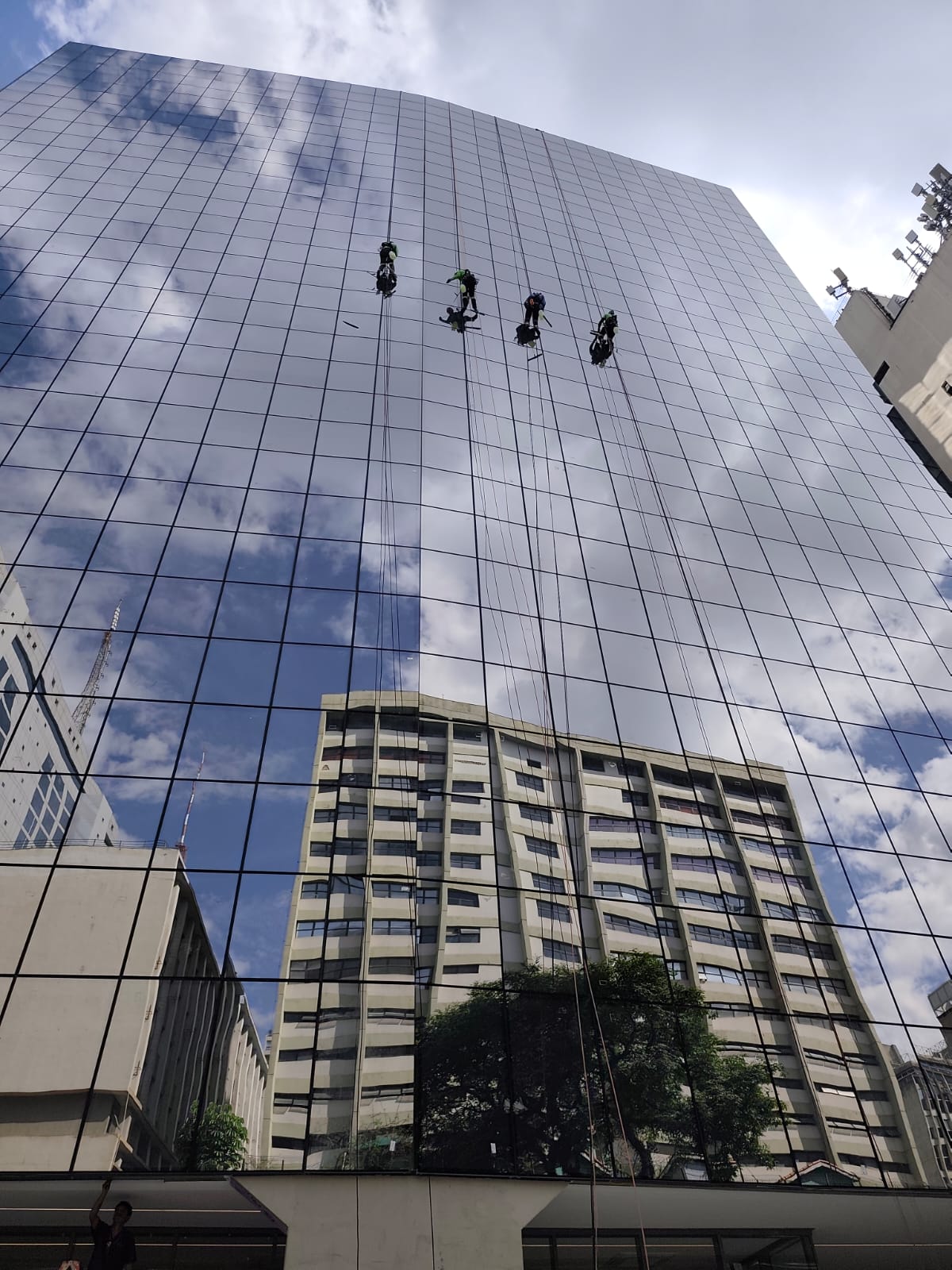 quatro profissionais da Fix Alt pendurados por cordas limpando a fachada de vidro espelhado de um prédio alto em São Paulo